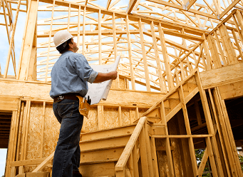 Construction worker wearing a hard hat reviews blueprints in the middle of a house that is being built